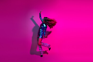 Vibrant celebration with a fashionable girl in a shiny blue dress dancing energetically against a pink neon background