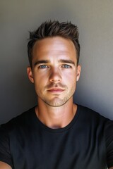Fototapeta premium Young man poses for a casual selfie against a neutral background showcasing his confident expression and stylish haircut