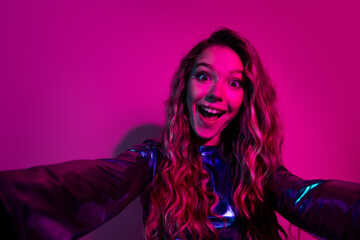 Young woman in a blue dress posing with a playful expression on a vibrant neon pink background