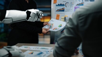 A striking image of a human and robot collaborating in a modern office setting, showcasing data analysis through charts and graphs for innovative presentation techniques.Noogenesis