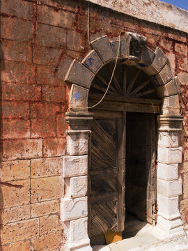 Charming Maroulas village, Rethymnon, Crete island, Greece.  Weathered, ornate old doorway in the old town. Rustic sunlit building. Vertical shot - no people.  Side view.