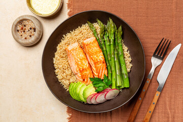Top view of plate with Salmon, Quinoa and Asparagus, redish and avocado on a mocha colour textile background, sauce.