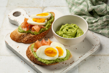 White wooden board with Smoked Salmon toast with Avocado cream. Sesame seeds bread, boiled egg. Close up of homemade sandwich.