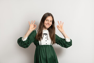 A woman with long brown hair is smiling while wearing a green dress with a white collar. She is...