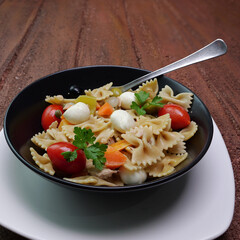 Piatto di pasta fredda con pomodori, olive, mozzarelle e sottaceti