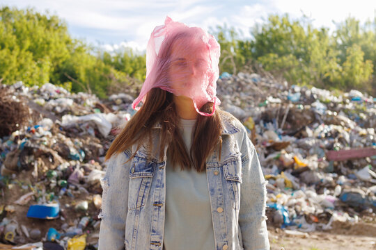 A woman with a plastic bag over her head stands at a landfill, symbolizing the suffocation and harm of plastic pollution on the environment.