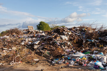 A large pile of mixed waste and garbage at a landfill site under a partly cloudy sky, illustrating environmental pollution.