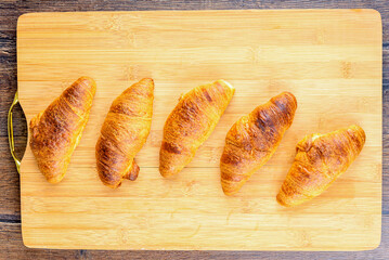 Top view of freshly baked croissants on wooden cutting board.