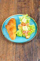 Lettuce, soft cheese and red fish with cucumber on half a croissant.