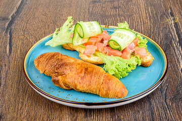 On half a croissant there is lettuce, soft cheese and red fish with cucumber.