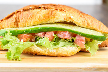 Close-up of croissant with lettuce, soft cheese and red fish with cucumber filling.