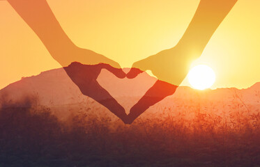 Hand shaped heart on beautiful golden sunset background.
