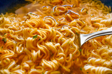 Instant noodles on fork in a bowl. Spicy noodle soup. Asian food style.