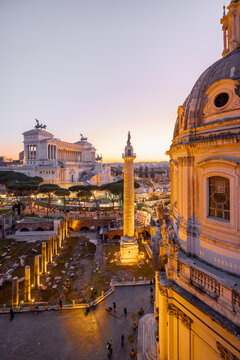 Scenic view of a historic dome and ancient Roman ruins glowing in the sunset light. The iconic Altare della Patria rises in the background above Romes evening skyline