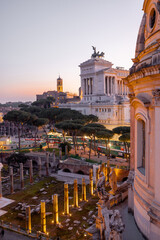 Obraz premium Scenic view of a historic dome and ancient Roman ruins glowing in the sunset light. The iconic Altare della Patria rises in the background above Romes evening skyline