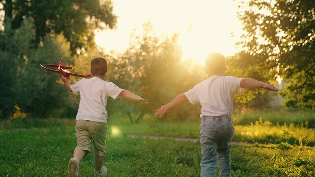 Boys, children are running with plane in their hands. Two children play with toy airplane in park in summer. Children boys play with toy airplane outdoor. Child dream is to fly, travel. Dream of - Powered by Adobe