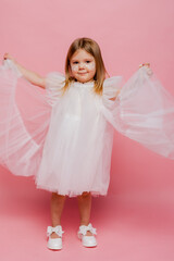 A little girl in a white fancy dress on a pink background in the studio