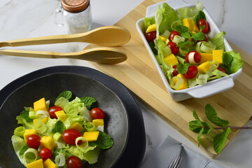 Salada tropical, com alface, manjericão, tomate cereja, manga servida em mesa com detalhes de decoração