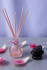 Fragrant reed diffuser with pink sticks and black stones on a gray surface decorated with rose...