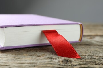 Book with red ribbon bookmark on wooden table against grey background, closeup