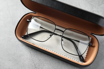 Case with stylish glasses and cleaning cloth on grey table, above view