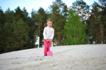 Cheerful child girl with two ponytails playing with shovel in the sand outdoor on nature in the spring. Happy childhood, outdoor activities, space for text