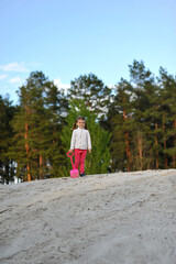 Child girl with two ponytails playing with shovel in the sand outdoor on nature in the spring. Outdoor activities. Copy space for text