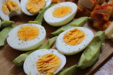 Close up with sliced boiled eggs and sliced avocado on a wooden board