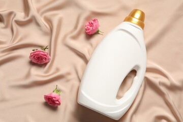 Bottle of fabric softener and flowers on beige cloth, flat lay