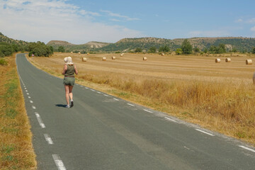 Obraz premium Woman walking along a road with bales of pressed straw in the background