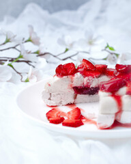 french dessert pavlova in section on a white plate with red strawberries on a white background