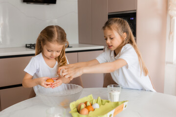Two little girls cook cookies at home in the kitchen
