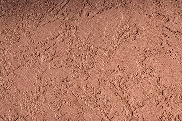 Close-up of a textured pink stucco wall with rough plaster patterns, ideal for backgrounds and architectural design uses.