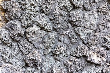 Close-up of a textured wall made of rough, porous volcanic rocks in natural light.