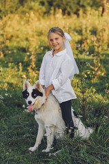 Smiling blond girl  with her pet dog outdooors on nature in summer. Yakutian Laika dog breed. Happy childhood