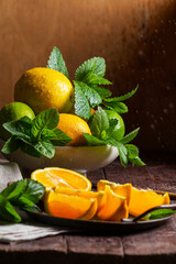 Oranges, lemons, limes, mint and lemon balm and raindrops illuminated by the sun on a wooden background.