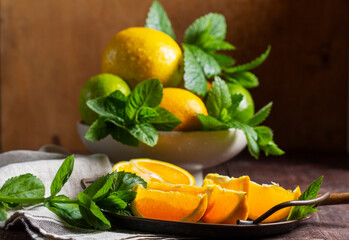 Oranges, lemons, limes, mint and lemon balm and raindrops illuminated by the sun on a wooden background.