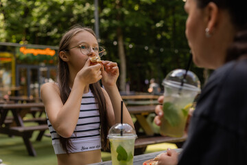 teenage girl drinks a cocktail and eats pizza in the summer at a cafe on the street
