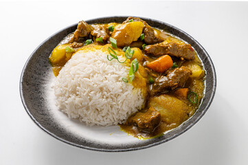 Beef curry rice with tender beef, creamy curry sauce, potatoes, carrots, and sticky rice, garnished with green onions in a rustic black bowl on a white background. 

