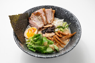 Miso ramen with noodles, pork belly, seaweed, greens, mushrooms, egg, and green onions in a rustic black bowl on a white background.
