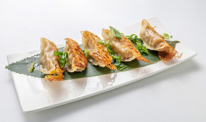 A tray of golden Yaki Gyoza, filled with pork and cabbage, served with soy sauce on a white background. A classic Asian dish showcasing Chinese and Japanese cuisine with a clean, minimal aesthetic.

