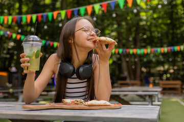 teenage girl drinks a cocktail and eats pizza in the summer at a cafe on the street