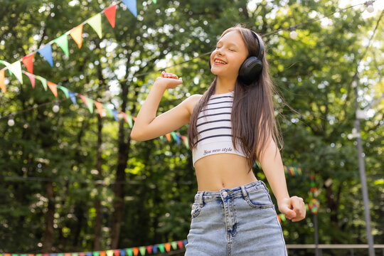 Happy teenage girl listens to music with headphones in summer park