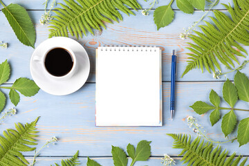 Summer composition with opened blank notepad, cup of black coffee, green leaves on wooden table....