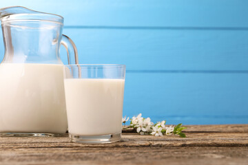 Fresh milk and blossoms on wooden table against light blue background, closeup. Space for text