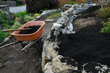 Landscape design project of stacked stone wall in progress in yard and garden