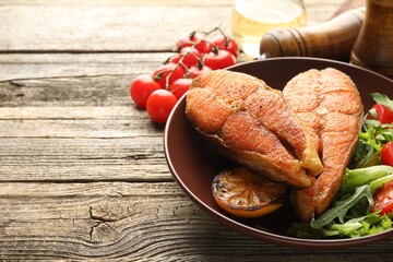 Seafood. Tasty salmon steaks served with salad and lemon on wooden table, closeup. Space for text