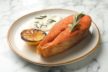 Seafood. Tasty salmon steak served with sauce, rosemary and lemon on white marble table, closeup