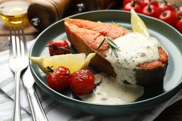 Seafood. Tasty salmon steak served with sauce, tomatoes, rosemary and lemon on table, closeup