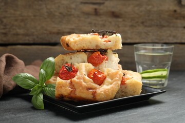 Pieces of delicious focaccia with tomatoes, basil and glass of water on gray table